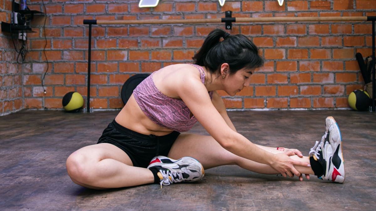 Woman performing stretches on gym floor, promoting exercise flexibility.